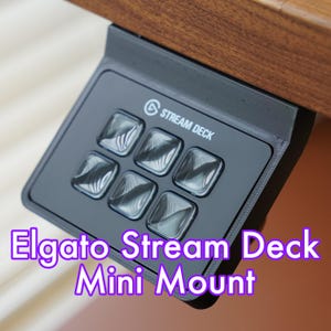 Może przedstawiać: Czarny Elgato Stream Deck Mini zamontowany na drewnianej powierzchni. Stream Deck Mini ma sześć przycisków z fakturowaną powierzchnią i napis "Stream Deck" nadrukowany z przodu.