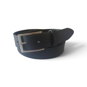 Peut inclure: Une ceinture noire à la texture lisse dotée d'une boucle rectangulaire en métal argenté. La ceinture est enroulée en forme circulaire, mettant en valeur la sangle, l'ardillon en métal, le cadre de la boucle et un passant en cuir noir assorti.