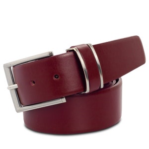Op de afbeelding: Een bordeauxrode leren riem met een zilverkleurige gesp en twee zilveren lussen. De riem is gemaakt van een glad materiaal en is ontworpen voor dagelijks gebruik. De gesp is rechthoekig en heeft een klassiek ontwerp.