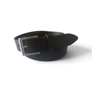 May include: A black belt featuring a smooth finish and a rectangular silver-toned metal buckle. The belt includes a single matching black leather loop and a pointed tip, coiled into a circular shape against a plain white background.