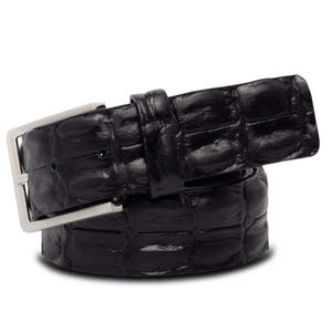 Puede incluir: Un cinturón de cuero negro con un patrón texturizado similar al de un cocodrilo. El cinturón presenta una hebilla rectangular de color plateado. Un accesorio clásico para pantalones o vaqueros.