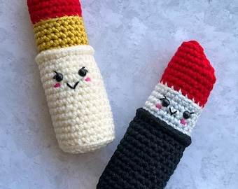 Puede incluir: Dos juguetes de labios de crochet con caras sonrientes. Uno es blanco con una banda amarilla y una parte superior roja, el otro es negro con una parte superior roja.