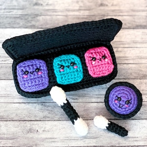 Puede incluir: Una paleta de maquillaje de ganchillo con tres sombras de ojos de colores y una pequeña esponja de maquillaje redonda de ganchillo. Cada sombra de ojos tiene una cara de dibujos animados linda con ojos y una sonrisa. También se incluyen dos bastoncillos de algodón negros y blancos.