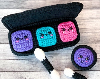 May include: A crocheted makeup palette with three colourful eyeshadows and a small, round, crocheted makeup sponge. Each eyeshadow has a cute, cartoon face with eyes and a smile. Two black and white cotton buds are also included.