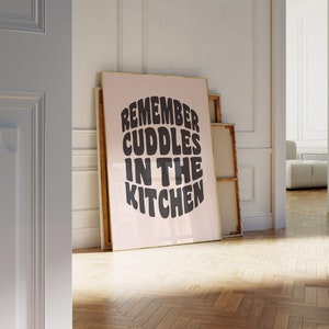 May include: A pink framed poster with the text "Remember cuddles in the kitchen" in black, stylized lettering.