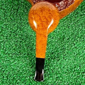 May include: A tobacco pipe featuring a polished, light brown burl wood bowl and stem with a distinct, textured grain pattern. The pipe includes a smooth, dark black acrylic mouthpiece attached to the end of the wooden stem, creating a contrast.