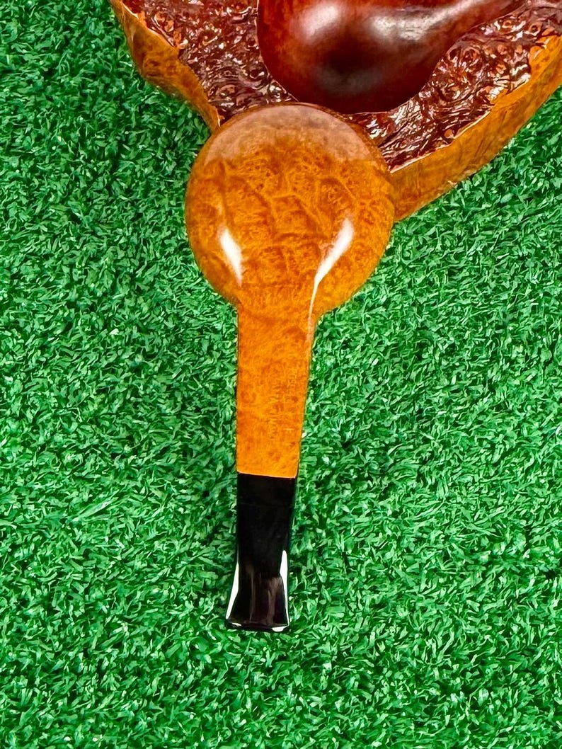May include: A tobacco pipe featuring a polished, light brown burl wood bowl and stem with a distinct, textured grain pattern. The pipe includes a smooth, dark black acrylic mouthpiece attached to the end of the wooden stem, creating a contrast.