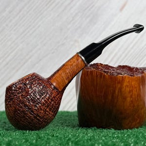 May include: A tobacco pipe with a dark brown, deeply textured bowl and a smooth, light brown shank featuring the engraved text 'Dr. Grabow' and 'MADE IN USA'. The pipe has a black stem and a silver-colored band at the connection point.