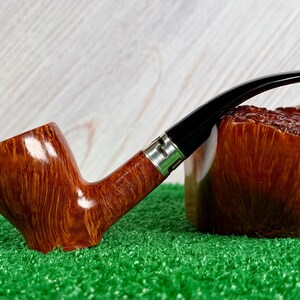 May include: A tobacco pipe with a polished, light brown wood grain bowl and a long, curved black stem. The pipe features a silver-colored metal band connecting the bowl to the stem, showcasing a smooth, glossy finish and a distinct wood texture.