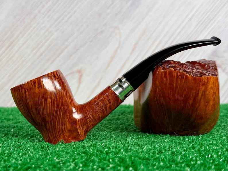May include: A tobacco pipe with a polished, light brown wood grain bowl and a long, curved black stem. The pipe features a silver-colored metal band connecting the bowl to the stem, showcasing a smooth, glossy finish and a distinct wood texture.