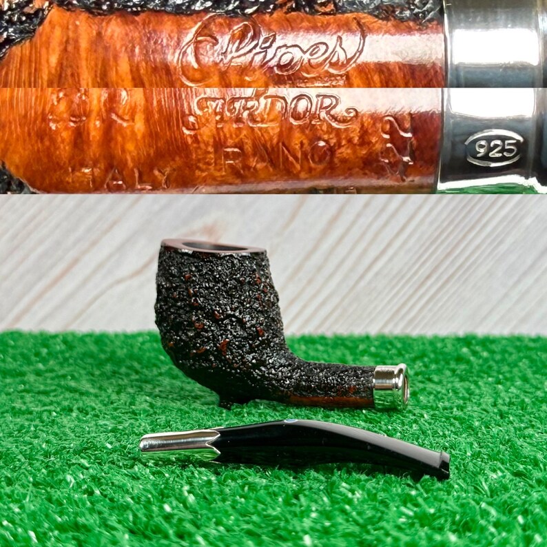 May include: A tobacco pipe with a dark, textured bowl and a curved stem. The pipe has a silver band and a separate black mouthpiece. The words "Pipes", "Srdor", "FRANCE", and "ITALY" are visible on the pipe.