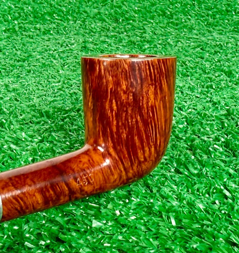May include: A polished brown tobacco pipe with a smooth, vertical wood grain pattern. The bowl is cylindrical with a flat rim, and the stem features the stamped text 457 near the transition point to the bowl, showing a glossy finish.