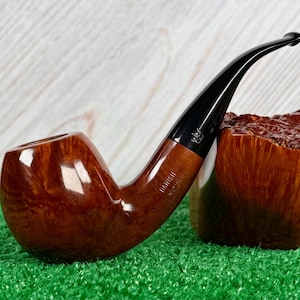 Pode incluir: Um cachimbo de tabaco curvo com uma tigela castanha e um bocal preto. O cachimbo tem uma forma arredondada e um acabamento polido. As palavras "Danish Natural" estão impressas na lateral. Um porta-tabaco de madeira está ao lado do cachimbo.