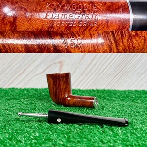 May include: A brown briar wood tobacco pipe with a detachable black stem. The pipe bowl is engraved with the text Kaywoodie Flame Grain Imported Briar and the number 45C. The stem features a silver-colored metal stinger attachment.