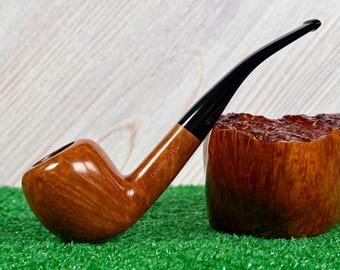 May include: A tobacco pipe with a polished light brown wooden bowl and a long, slender black stem. The word CONNOISSEUR is stamped into the side of the wooden shank. The pipe is positioned next to a large, textured, dark brown wooden block.