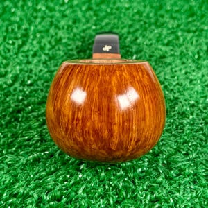 May include: A polished tobacco pipe bowl crafted from light brown wood with a visible grain pattern. The pipe features a smooth, rounded shape and a black stem attachment at the top, which is marked with the letters jp in a white font.