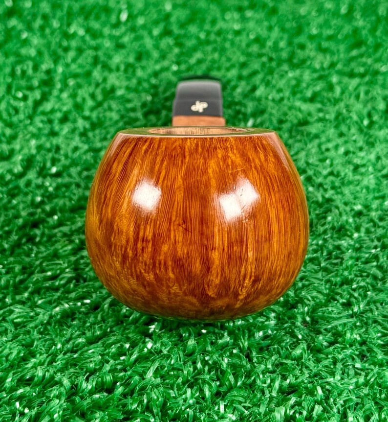 May include: A polished tobacco pipe bowl crafted from light brown wood with a visible grain pattern. The pipe features a smooth, rounded shape and a black stem attachment at the top, which is marked with the letters jp in a white font.