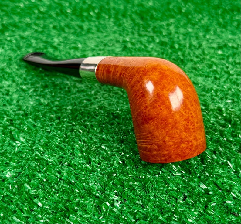 Puede incluir: Una pipa de tabaco con un hornillo de madera de color marr&oacute;n claro pulido con un patr&oacute;n de veta visible, conectado a una boquilla negra lisa mediante una banda de metal de color plateado. La pipa est&aacute; colocada horizontalmente.