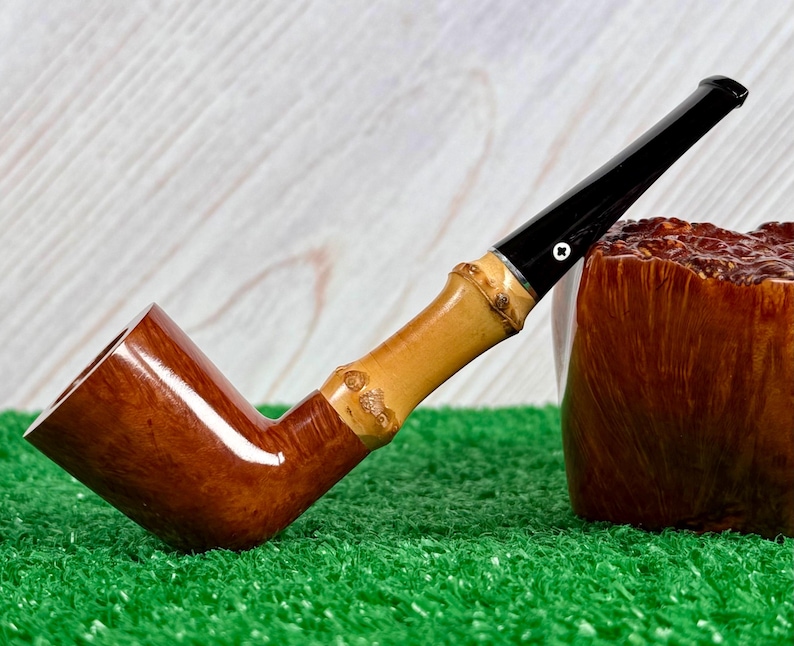 May include: A wooden tobacco pipe with a bamboo stem and a black mouthpiece. The pipe has a curved design and rests on a green surface. A brown, textured object is next to the pipe.