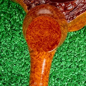 May include: A tobacco pipe featuring a polished, light brown briar wood bowl with a distinct burl grain pattern. The stem is connected to a silver-colored metal band, and the wood surface displays a smooth, glossy finish with visible natural textures.