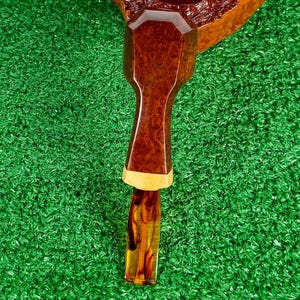 Pode incluir: Um cachimbo de tabaco com fornilho de madeira castanho-escura polida com um padr&atilde;o de gr&atilde;o de madeira texturizado. A haste &eacute; composta por uma sec&ccedil;&atilde;o de madeira castanha facetada ligada a um anel de madeira clara e uma boquilha de acr&iacute;lico &acirc;mbar transl&uacute;cido.