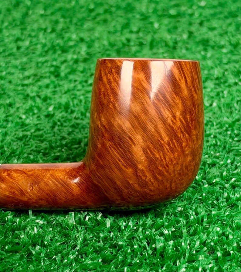 Op de afbeelding: Een gepolijste bruine tabakspijp met een gladde, glanzende afwerking en zichtbare houtnerfpatronen. De pijp heeft een cilindrische kop en een horizontale steel, met een rijke, warme amberkleur over het gehele houten oppervlak.