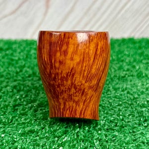 May include: A smooth, polished tobacco pipe bowl featuring a rich, warm amber-brown wood grain pattern. The bowl has a rounded, slightly tapered cylindrical shape with a visible, dark-toned interior opening at the top and a smooth finish.