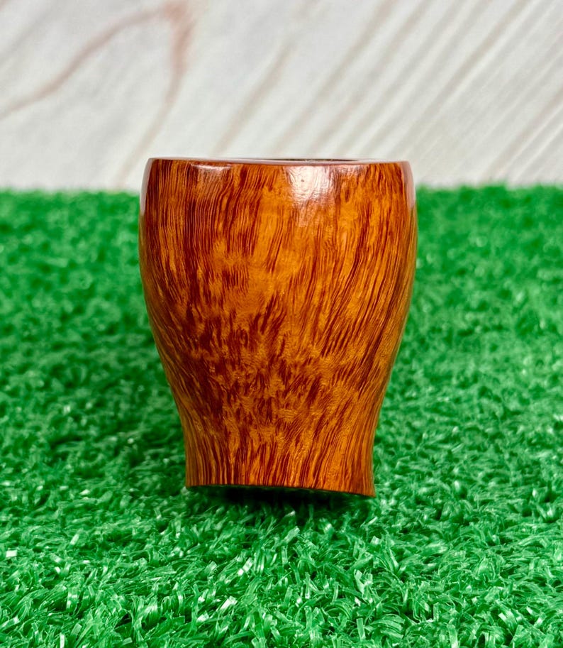 May include: A smooth, polished tobacco pipe bowl featuring a rich, warm amber-brown wood grain pattern. The bowl has a rounded, slightly tapered cylindrical shape with a visible, dark-toned interior opening at the top and a smooth finish.