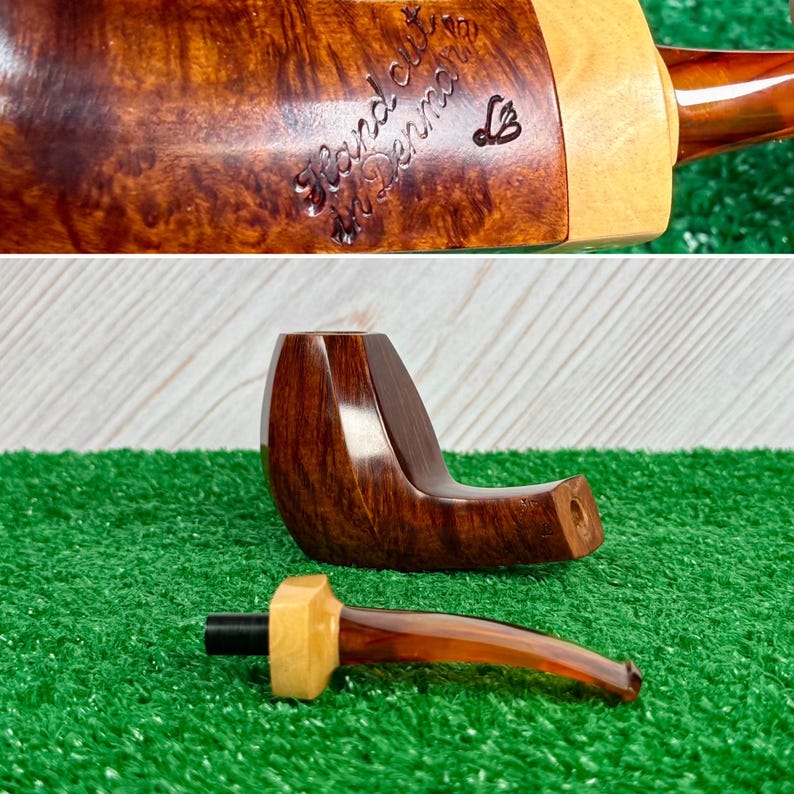 Pode incluir: Um cachimbo de tabaco com um fornilho de madeira castanho-escura polida com veios e uma piteira destac&aacute;vel com um detalhe em madeira clara e uma ponta de cor &acirc;mbar transl&uacute;cida. O fornilho tem gravado o texto Hand cut in Denmark e um log&oacute;tipo.