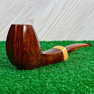 Pode incluir: Um cachimbo de tabaco com fornilho de madeira castanho-escuro polido e design facetado. A piteira &eacute; feita de um material transl&uacute;cido de cor &acirc;mbar e est&aacute; ligada ao fornilho por um anel de madeira clara e lisa que acentua a transi&ccedil;&atilde;o.