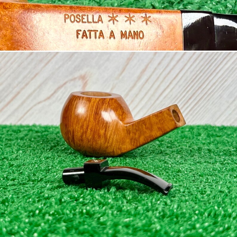 May include: A light brown wooden tobacco pipe with a smooth finish and a detachable black stem. The bowl is engraved with the text POSELLA *** FATTA A MANO. The pipe is shown in two parts, with the bowl and the stem separated on a green surface.