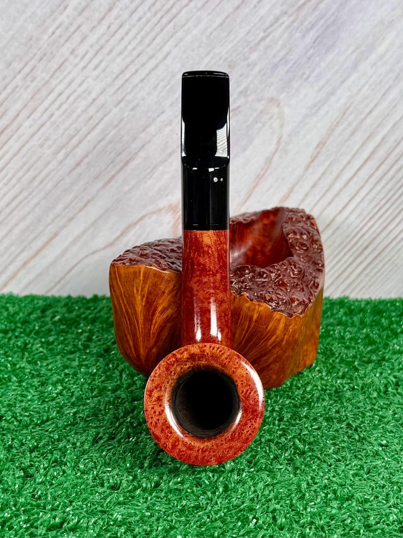 May include: A tobacco pipe featuring a polished, reddish-brown wooden bowl with a textured, rustic finish and a smooth, cylindrical stem. The pipe includes a glossy black acrylic mouthpiece attached to the shank, presented in a vertical orientation.