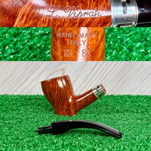 May include: A brown briar wood tobacco pipe with a smooth, polished finish and a silver-colored metal band. The pipe is engraved with the text L. Viprati, HAND MADE ITALY, and two small symbols. A separate black acrylic stem is positioned below.
