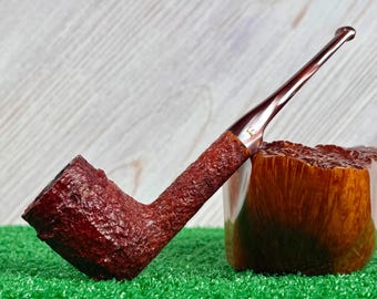 May include: A tobacco pipe with a dark reddish-brown, deeply textured bowl and shank. The stem is smooth, glossy, and dark brown, featuring a small gold-colored letter E logo near the junction with the shank. The pipe is positioned upright.