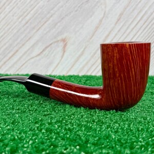 May include: A tobacco pipe featuring a polished reddish-brown wooden bowl with a visible natural grain pattern. The pipe has a smooth, curved black acrylic stem that connects to the bowl, presenting a classic L-shaped profile for smoking tobacco.