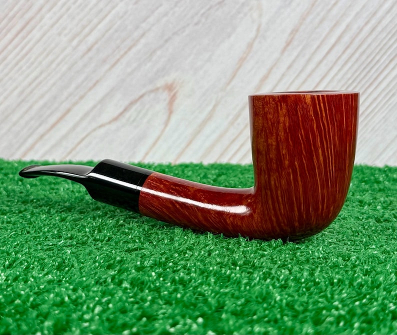 May include: A tobacco pipe featuring a polished reddish-brown wooden bowl with a visible natural grain pattern. The pipe has a smooth, curved black acrylic stem that connects to the bowl, presenting a classic L-shaped profile for smoking tobacco.