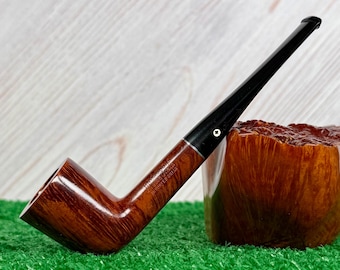 May include: A brown wooden tobacco pipe with a long black stem and a silver-colored metal band. The pipe features a smooth, polished finish and includes the stamped text "BRUYERE GARANTIE" and "IMPORTE D'BRIAR" on the side of the bowl.