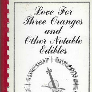 Könnte beinhalten: Ein Kochbuch mit dem Titel "Love For Three Oranges and Other Notable Edibles" mit roter Spiralbindung. Das Cover zeigt eine Geige in einem Notenlinienkreis. Der Text "The Indiana University String Academy Cookbook" steht unten.