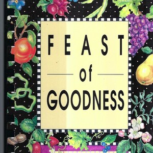 May include: A black and white cookbook with a yellow cover titled "Feast of Goodness" with a pink and white label that says "Piedmont Carolinas AACN". The cover is decorated with various fruits, vegetables, and flowers.
