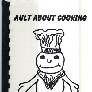 Op de afbeelding: Een zwart-witte illustratie van een kok met een koksmuts en een glimlach. De tekst "AULT ABOUT COOKING" staat bovenaan de afbeelding. De tekst "Gregory Gustafson" staat onderaan de afbeelding.