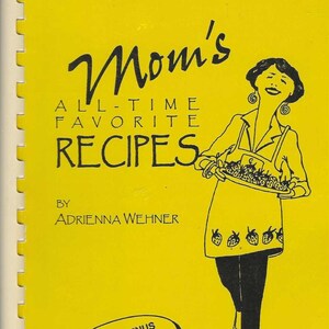 Puede incluir: Portada de libro de cocina vintage con fondo amarillo. El título dice "Mom's All-Time Favorite Recipes" en escritura negra. Se presenta una ilustración de una mujer sosteniendo una bandeja de comida. El autor es "Adrienna Wehner". Una burbuja de texto dice "Variety Menus in Less Time".