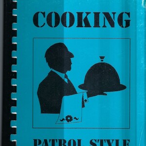 Puede incluir: Un libro de cocina azul con una silueta negra de un camarero sosteniendo una campana. El título es "Cooking Patrol Style" y el subtítulo es "By the Patrols of Crossfield 1993-1994".