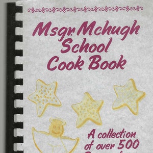 May include: A spiral-bound cookbook titled "Msgr. Mchugh School Cook Book" with a light background. The cover features illustrations of star-shaped biscuits and an angel-shaped biscuit. Text reads "A collection of over 500 Recipes from Family, Faculty and local Restaurants."
