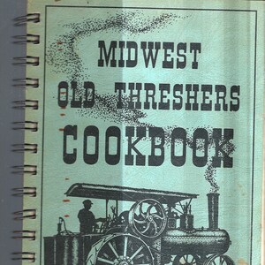 Può includere: Un ricettario verde intitolato "Midwest Old Threshers Cookbook" con un'illustrazione in bianco e nero di un motore a vapore d'epoca sulla copertina. Il libro è stato pubblicato a Mt. Pleasant, Iowa nel 1982.