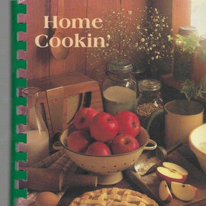 May include: A cookbook titled "Home Cookin'" with a pie, apples, eggs, and jars of ingredients. The cookbook is titled "Our Daily Bread" and is compiled by Montgomery Evangelical Free Church.