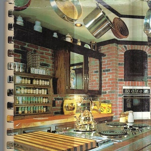 Könnte beinhalten: Ein Vintage-Kochbuch mit einem rot-weiß-blauen Umschlag mit dem Text "Favorite Recipes from our Best Cooks COOK BOOK". Der Umschlag zeigt eine Küche mit einer Backsteinwand, einem Holzschrank und einem Herd mit einem Schneidebrett.