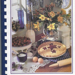 May include: A cookbook titled "Our Favorite Recipes from Pinedale Baptist Church" with a photo of a pie, cherries, and other baking ingredients on a table with a window in the background.