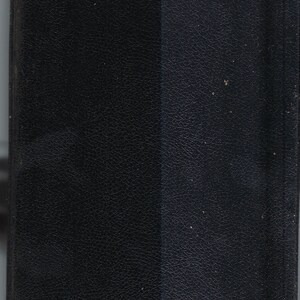 May include: A black leather-bound book with a textured surface. The cover is divided into two vertical sections, with a slight color variation between them. The book appears to be closed and in good condition.