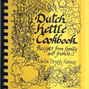 Könnte beinhalten: Ein gelbes Kochbuch mit dem Titel "Dutch Kettle Cookbook" mit schwarzem Text und Illustrationen von Gemüse und Pflanzen. Auf dem Cover steht "Rezepte von Familie und Freunden" und der Name der Autorin, Adella Brunk Kanagy.