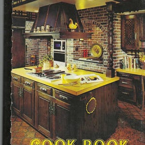 May include: A vintage cookbook cover with a photo of a kitchen with a yellow countertop and brown cabinets. The text on the cover reads "Cook Book Favorite Recipes From Our Best Cooks".